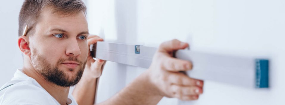 Worker with pencil behind his ear checking if the wall is straight with a spirit level